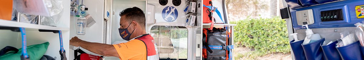 Profile of a first aid worker with mask working with a desfibrillator bag inside an ambulance